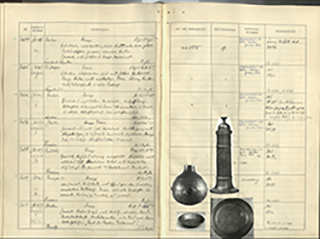 aufgeschlagenes Buch von oben mit handschriftlichen Einträgen und eingeklebten Schwarz-weiß-Fotos von Objekten